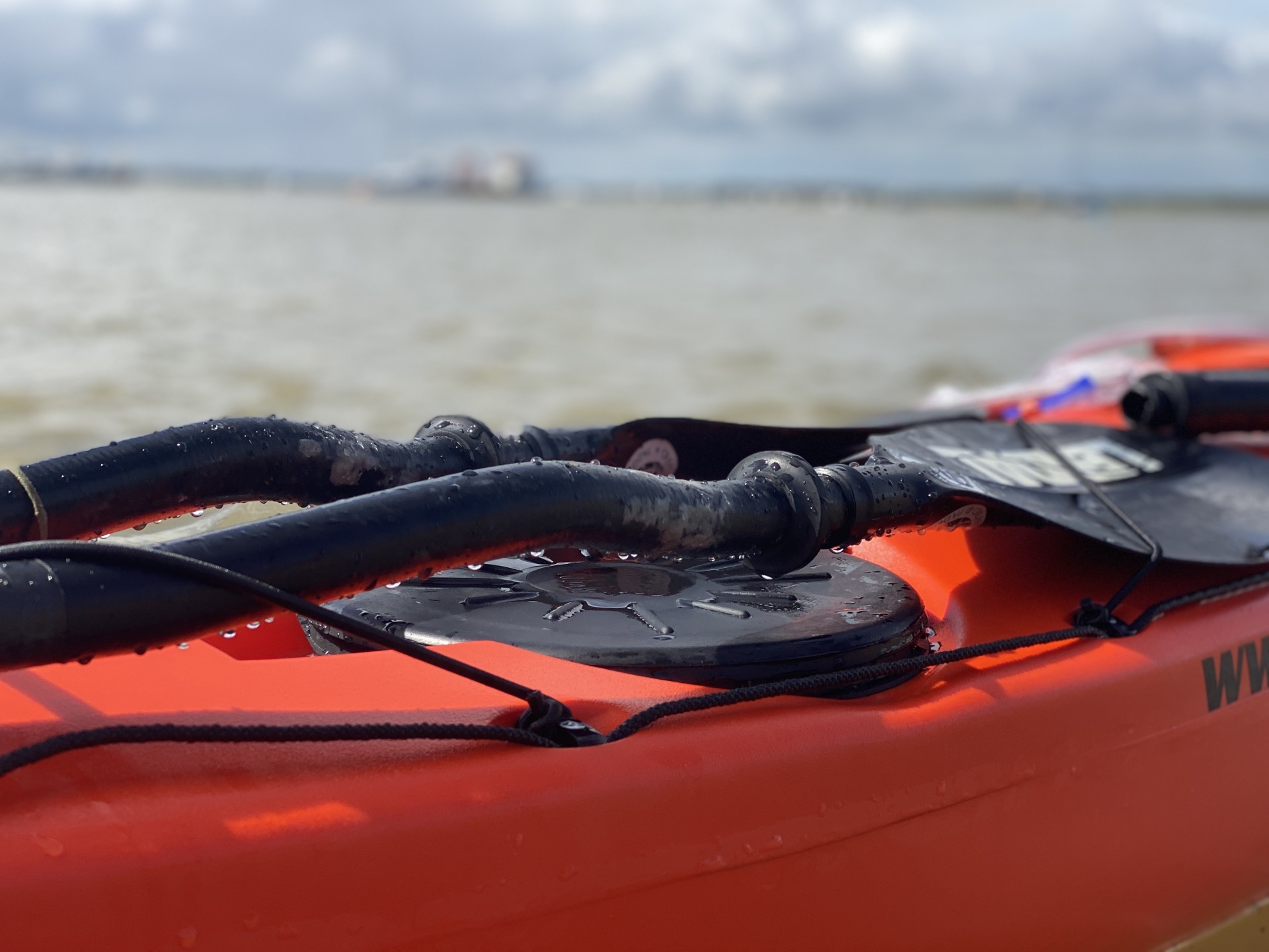 Split paddles on the front deck of an orange sea kayak.